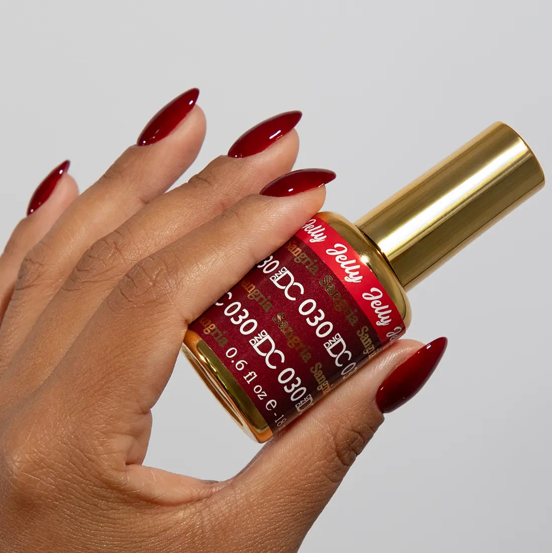 Hand with long almond nails wearing DC Jelly Sangria deep berry red jelly nail polish, holding a bottle of DND nail polish