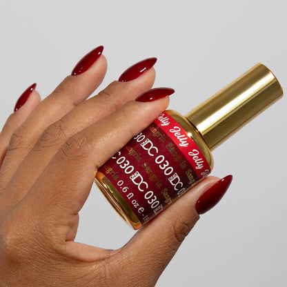 Hand with long almond nails wearing DC Jelly Sangria deep berry red jelly nail polish, holding a bottle of DND nail polish