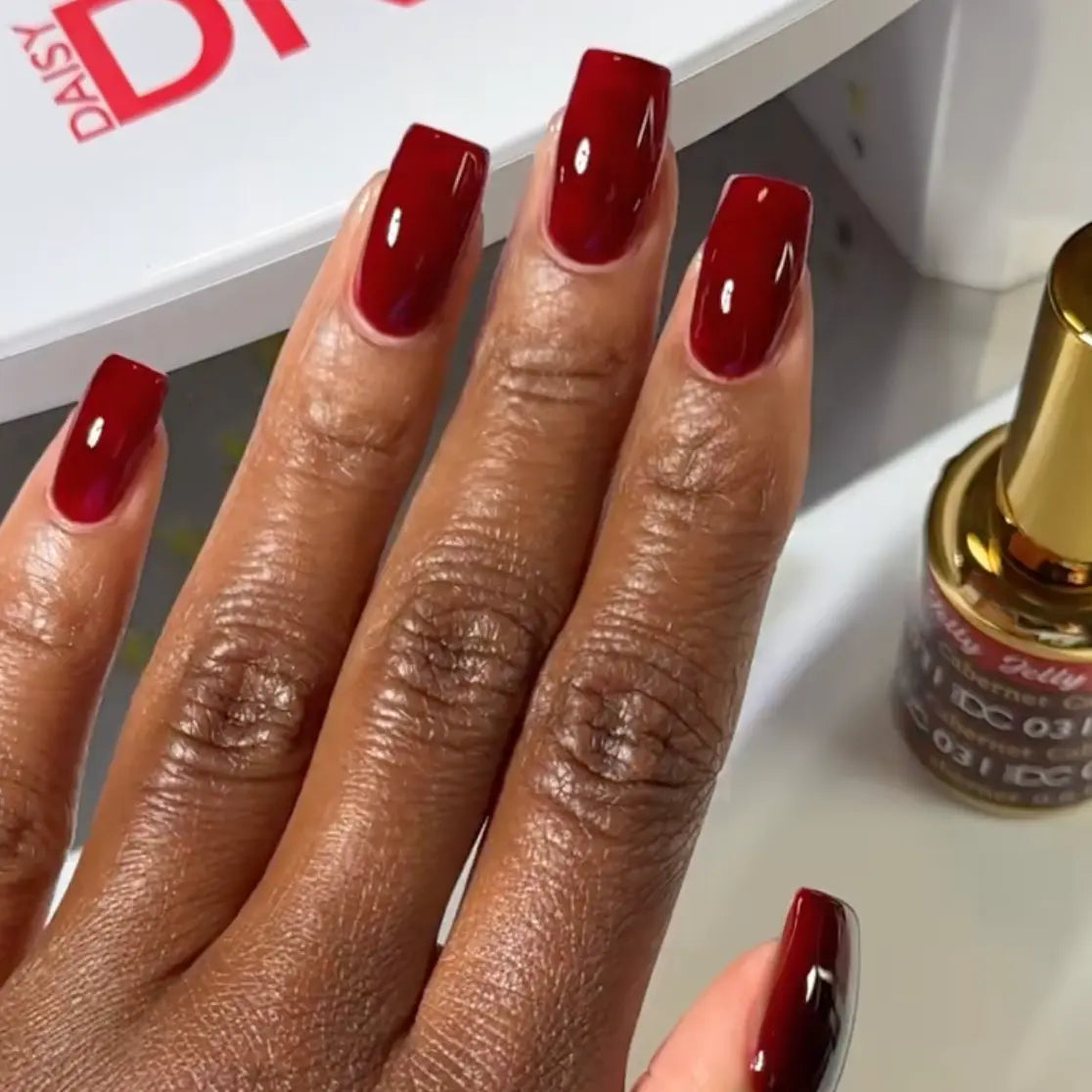 Hand with long square nails wearing DC Jelly Cabernet deep burgundy wine jelly nail polish