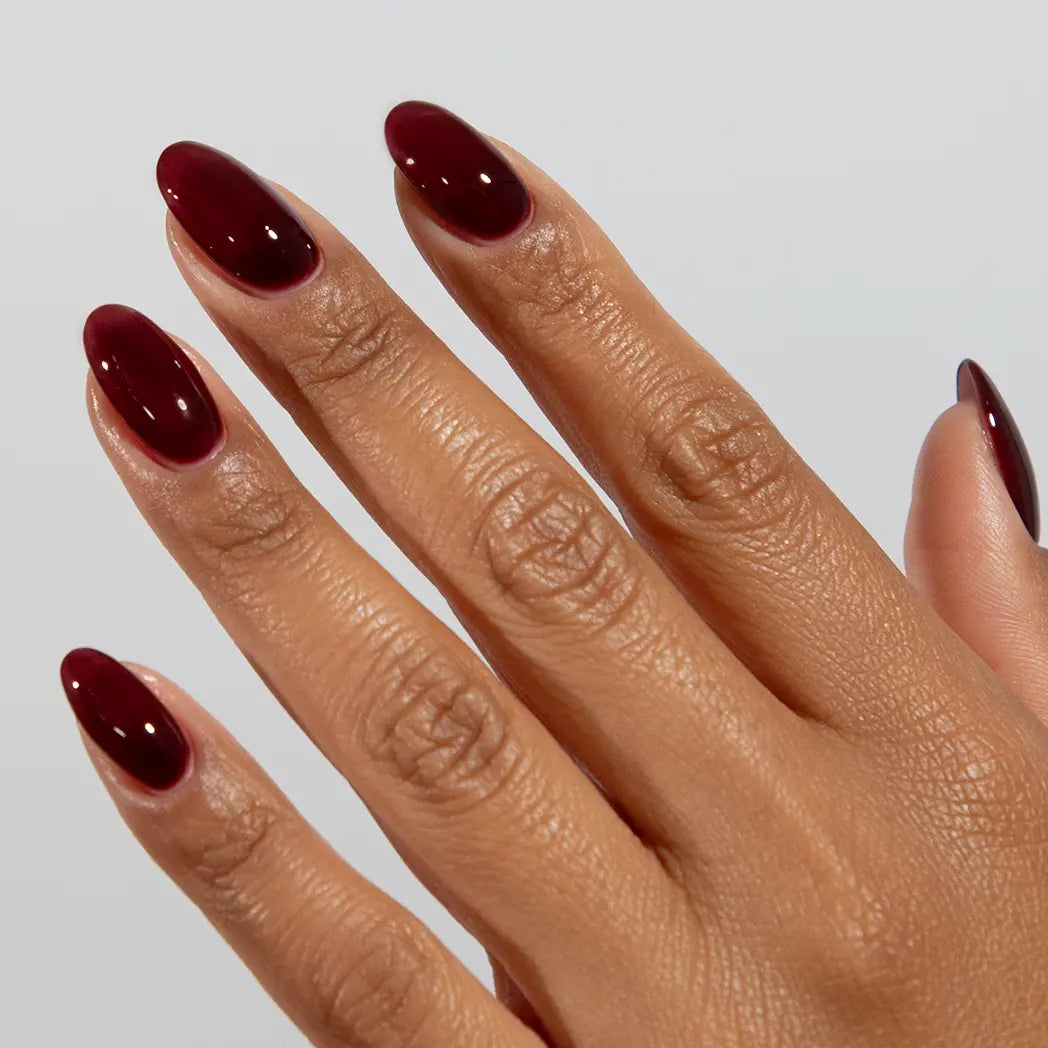 Hand with long almond nails wearing DC Jelly Vineyard deep cinnamon red jelly nail polish with a purple flush