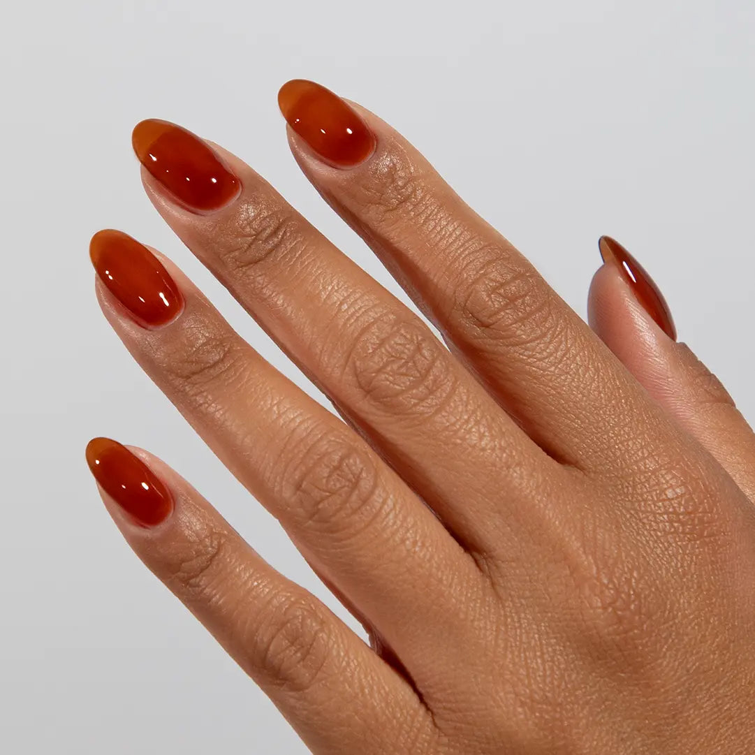 Close-up of a hand with long almond-shaped nails wearing DC Jelly Caramel burnt-honey orange-brown jelly nail polish