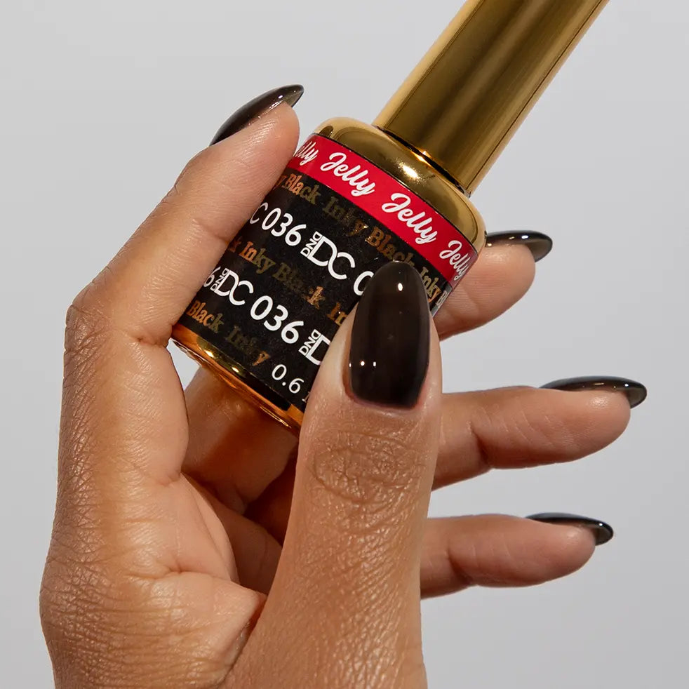 Hand with long stiletto nails wearing DC Jelly Inky Black jelly nail polish, holding a bottle of DND nail polish