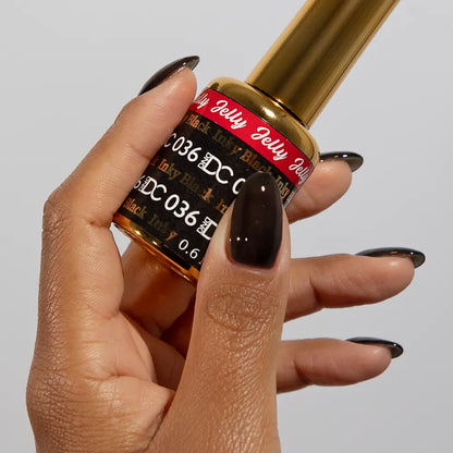 Hand with long stiletto nails wearing DC Jelly Inky Black jelly nail polish, holding a bottle of DND nail polish