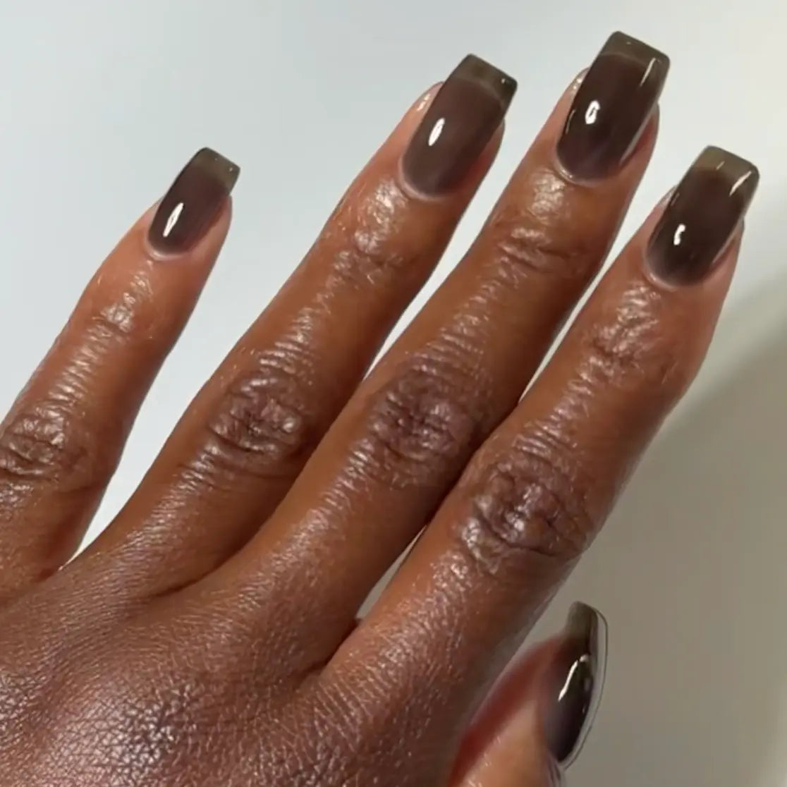 Hand with square nails wearing DC Jelly Inky Black translucent black-brown jelly nail polish