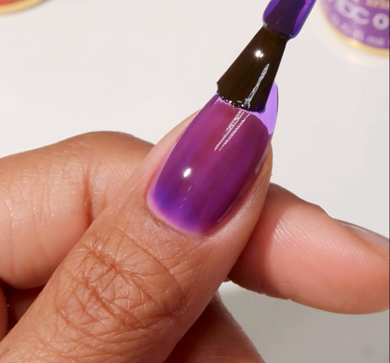 Brush applying glossy DC Jelly Iris purple jelly gel nail polish to a fingernail