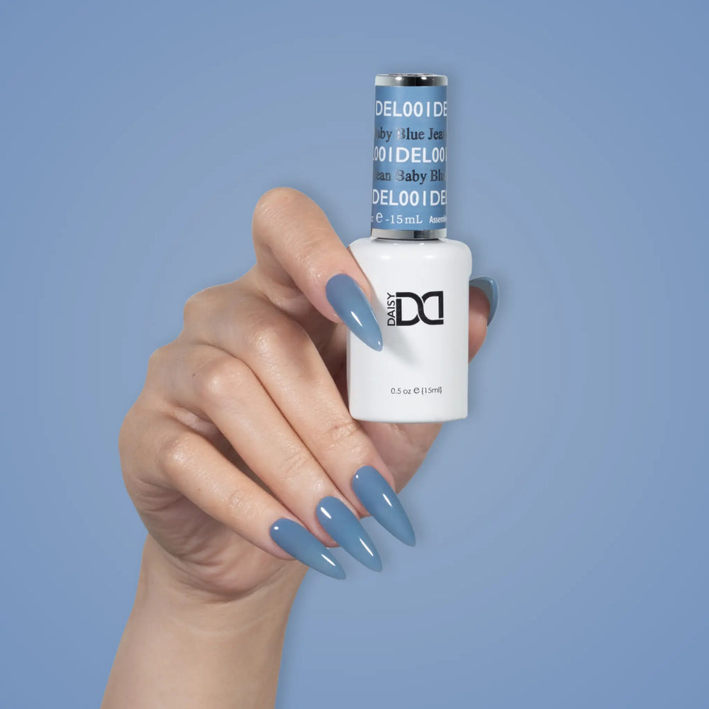 Hand with glossy slate blue nails holding a DND DEL #001 Baby Blue Jean gel polish bottle
