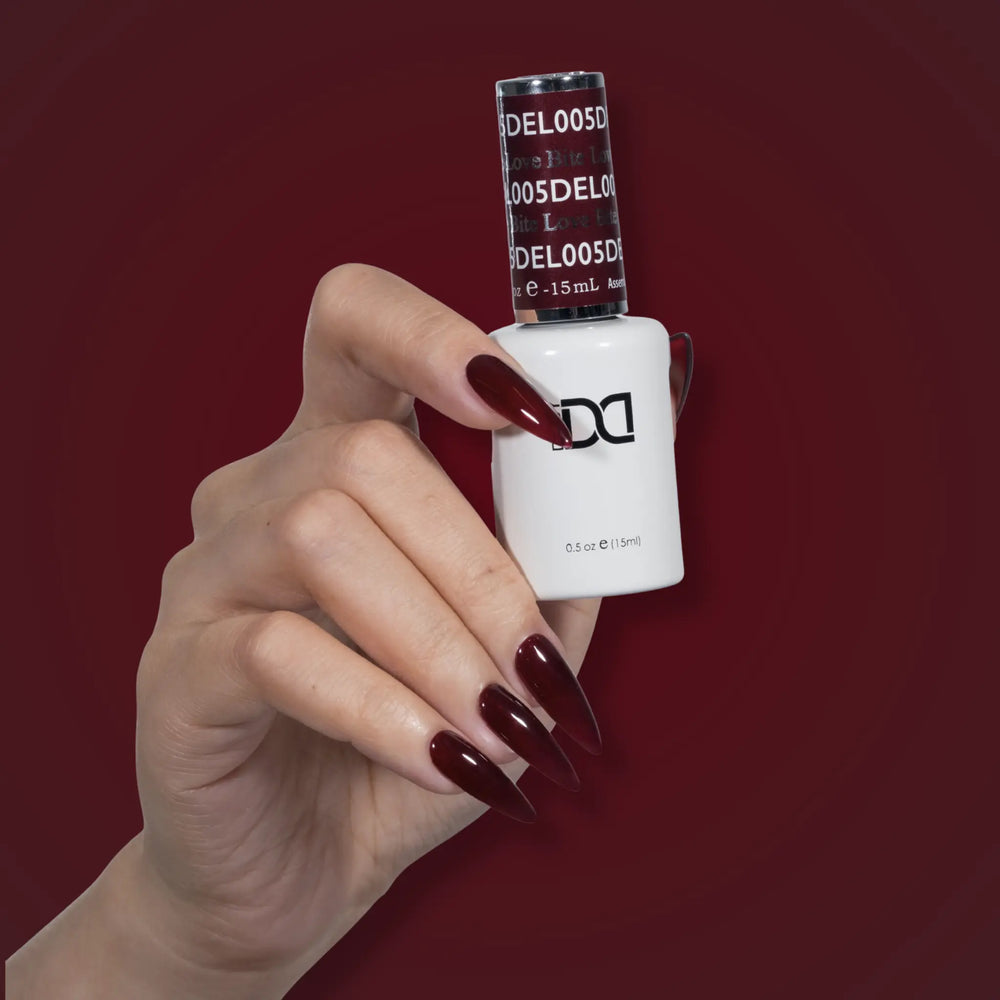 Hand with glossy dark red nails holding a DND DEL #005 Love Bite gel polish bottle