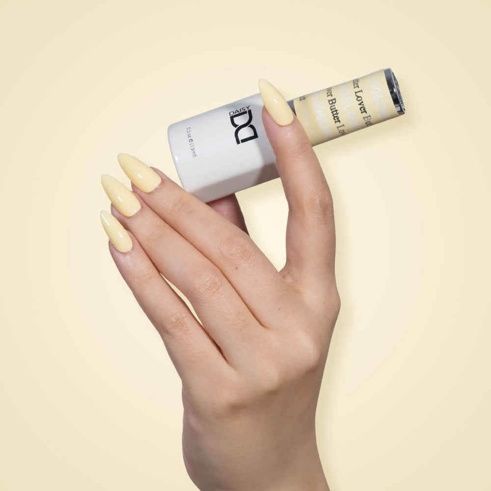 Hand with glossy pale yellow nails holding a DND DEL #006 Butter Lover gel polish bottle