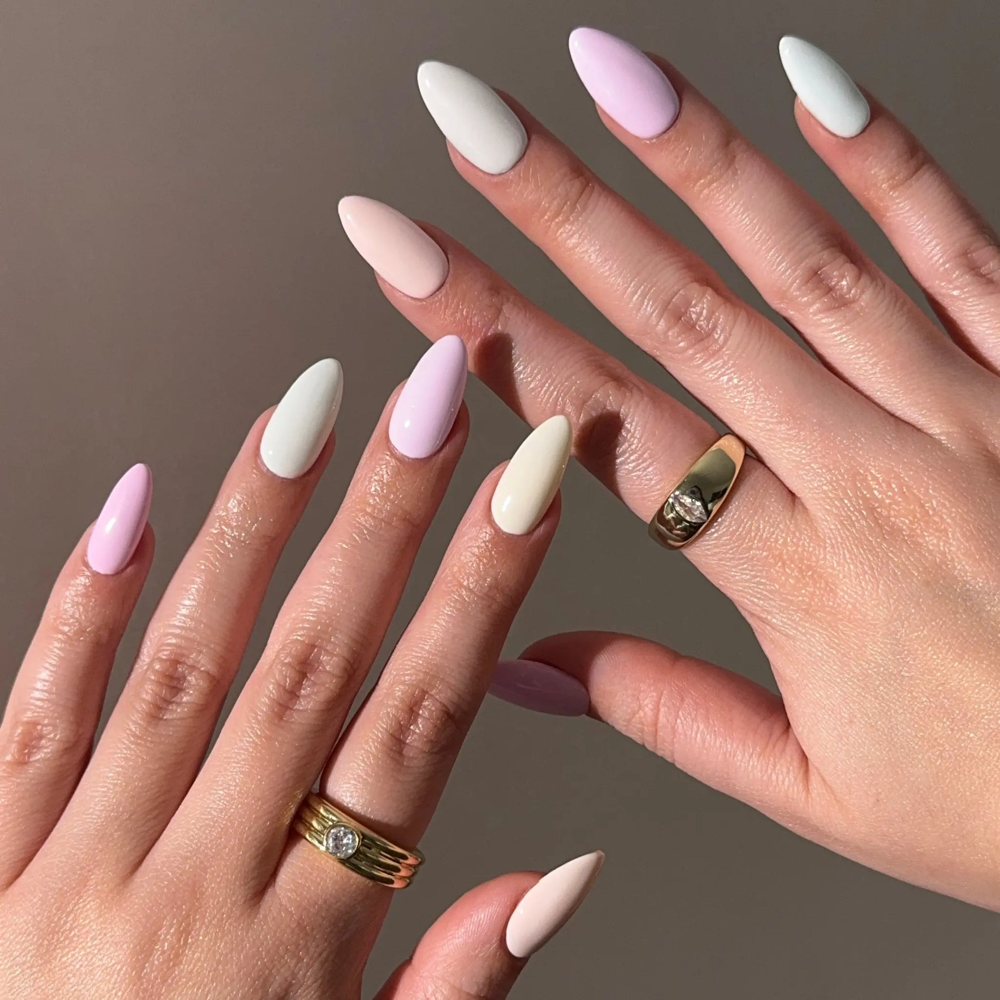 Close-up of hands with pastel pink, cream, and white nail colors on a neutral background