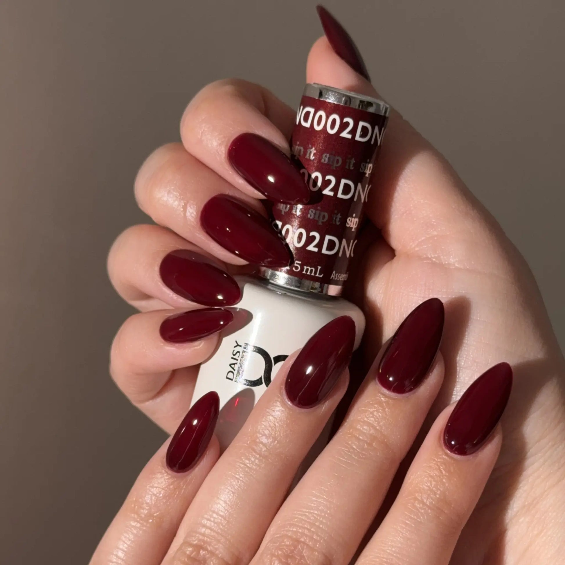 Hand with warm red nail polish holding a bottle of DND nail polish.