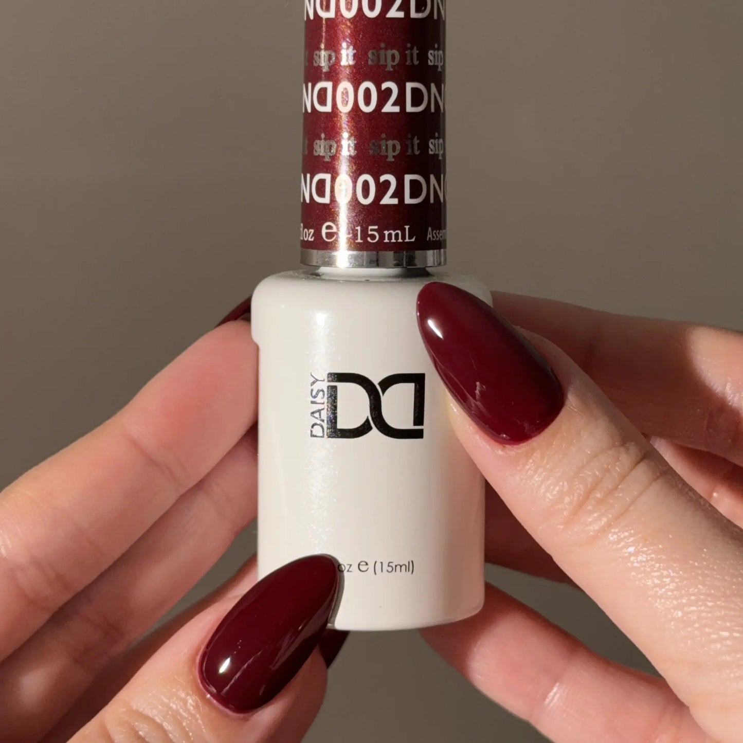 Hand holding a bottle of DND nail polish with a matching wine red nail color.