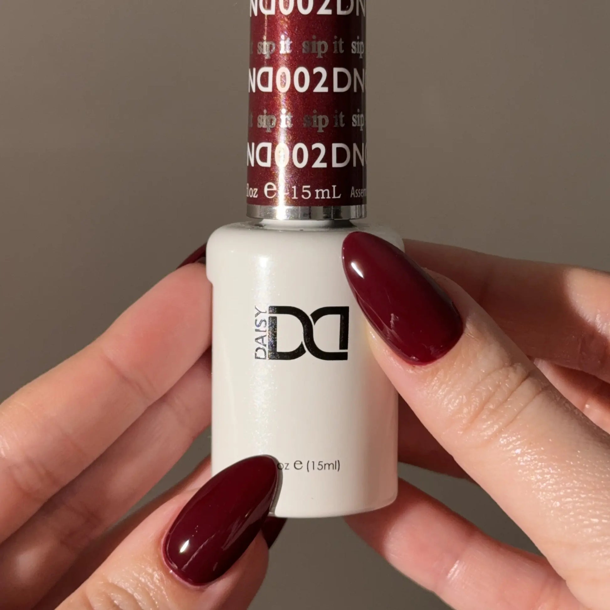 Hand holding a bottle of DND nail polish with a matching wine red nail color.