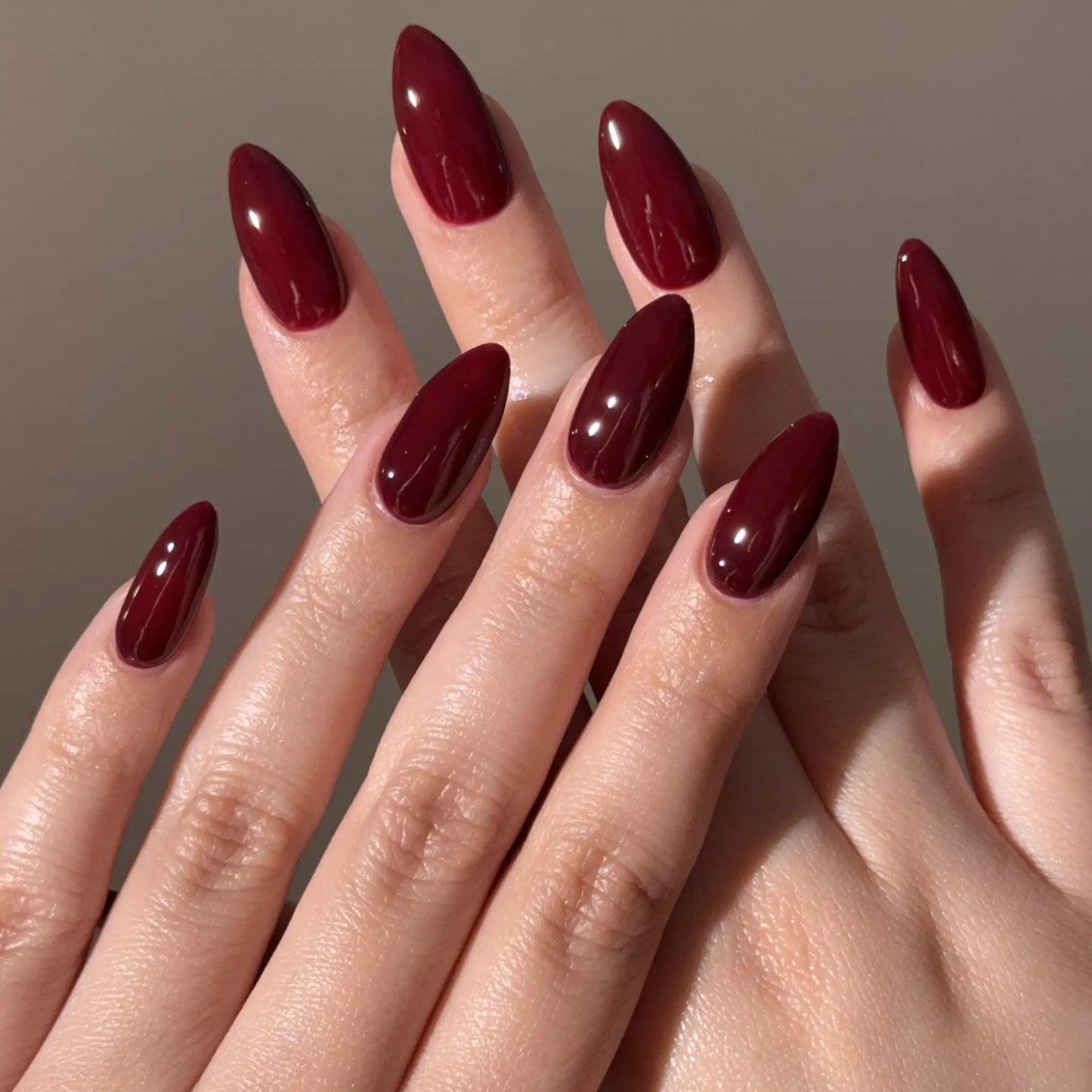 Close-up of a hand with wine red nail polish on a neutral background
