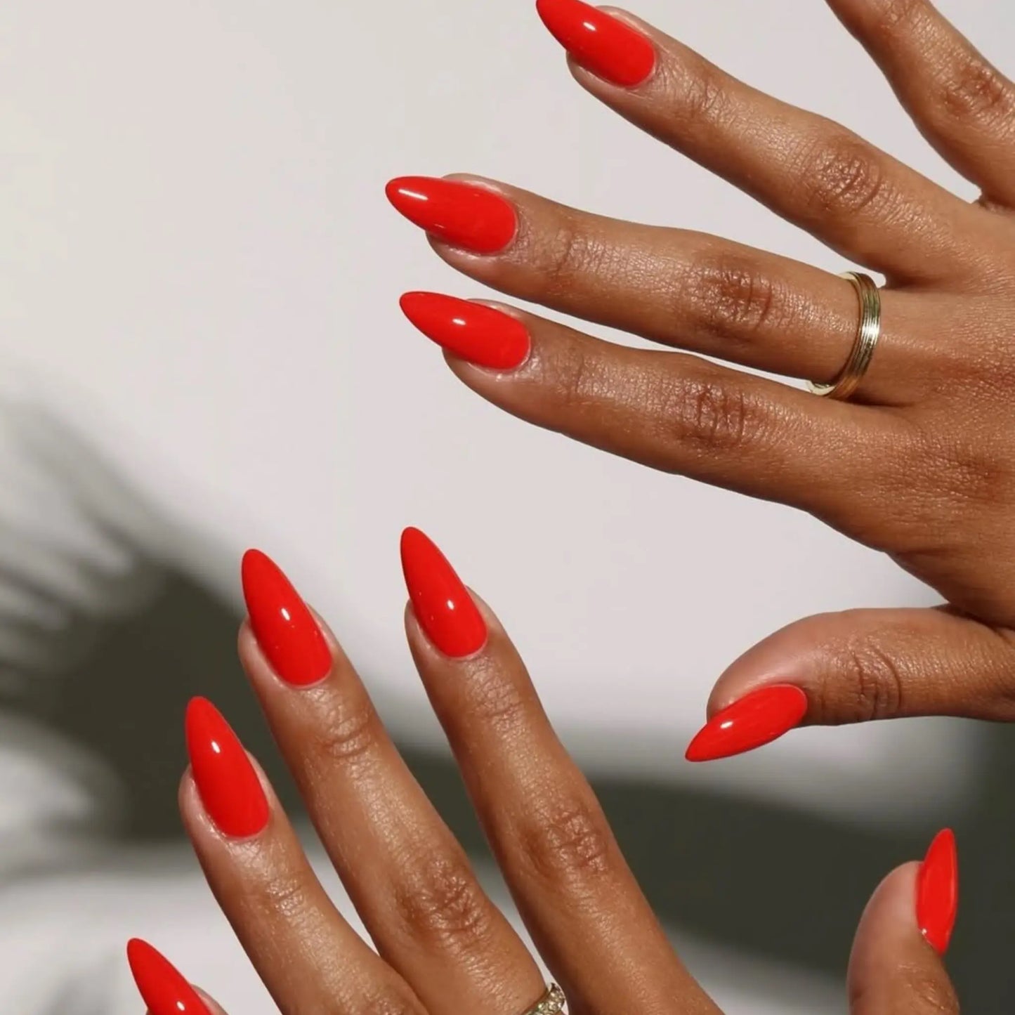 Two hands with long stiletto nails wearing SCORCHING glossy warm red nail polish