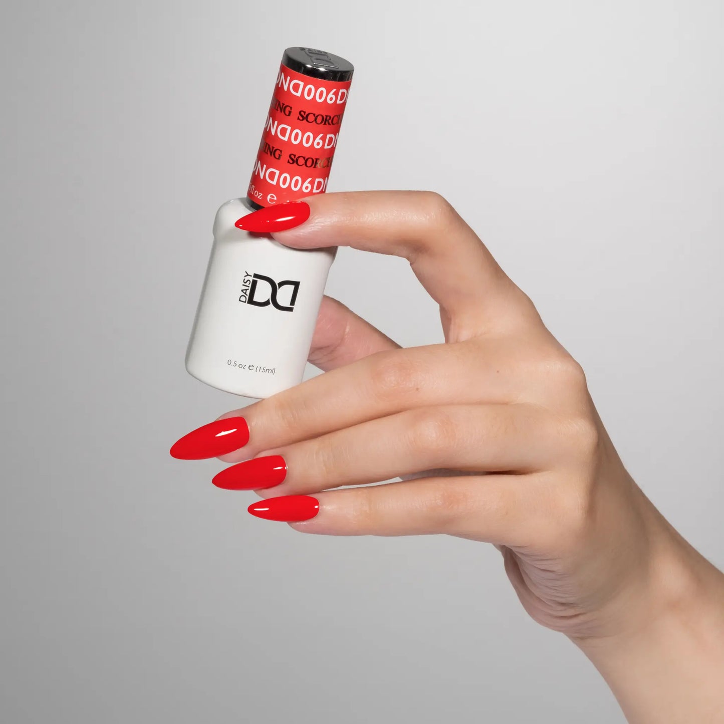 Hand with red stiletto nails holding a bottle of DND Scorching nail polish #006