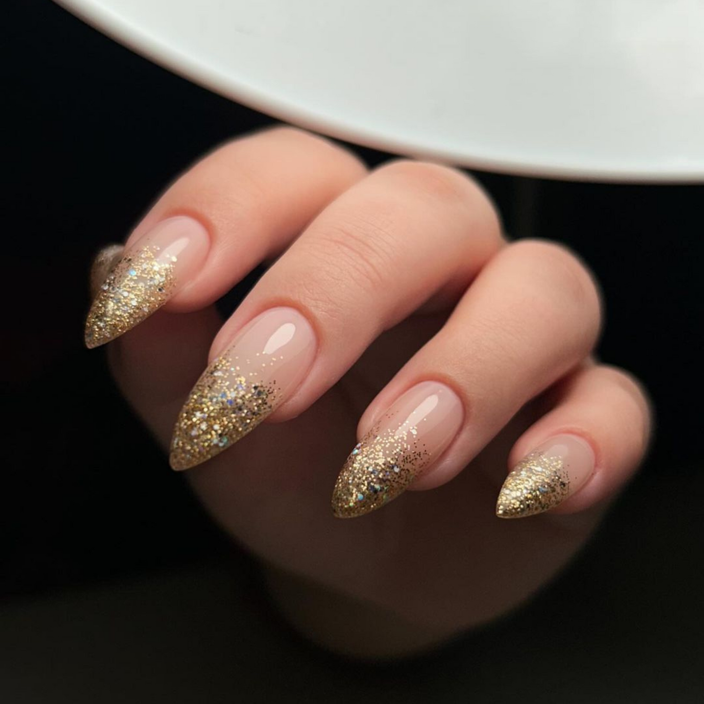Hand with medium stiletto nails wearing Golden Shara Star gold glitter nail polish in an ombre french tip