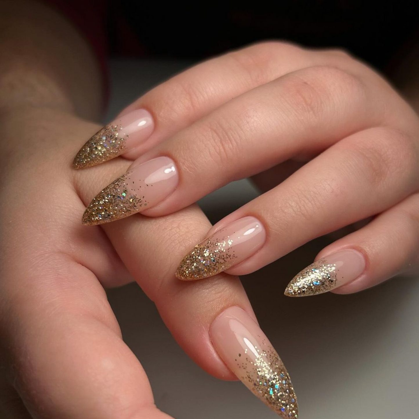 Hand with medium stiletto nails wearing Golden Shara Star gold glitter nail polish in an ombre french tip