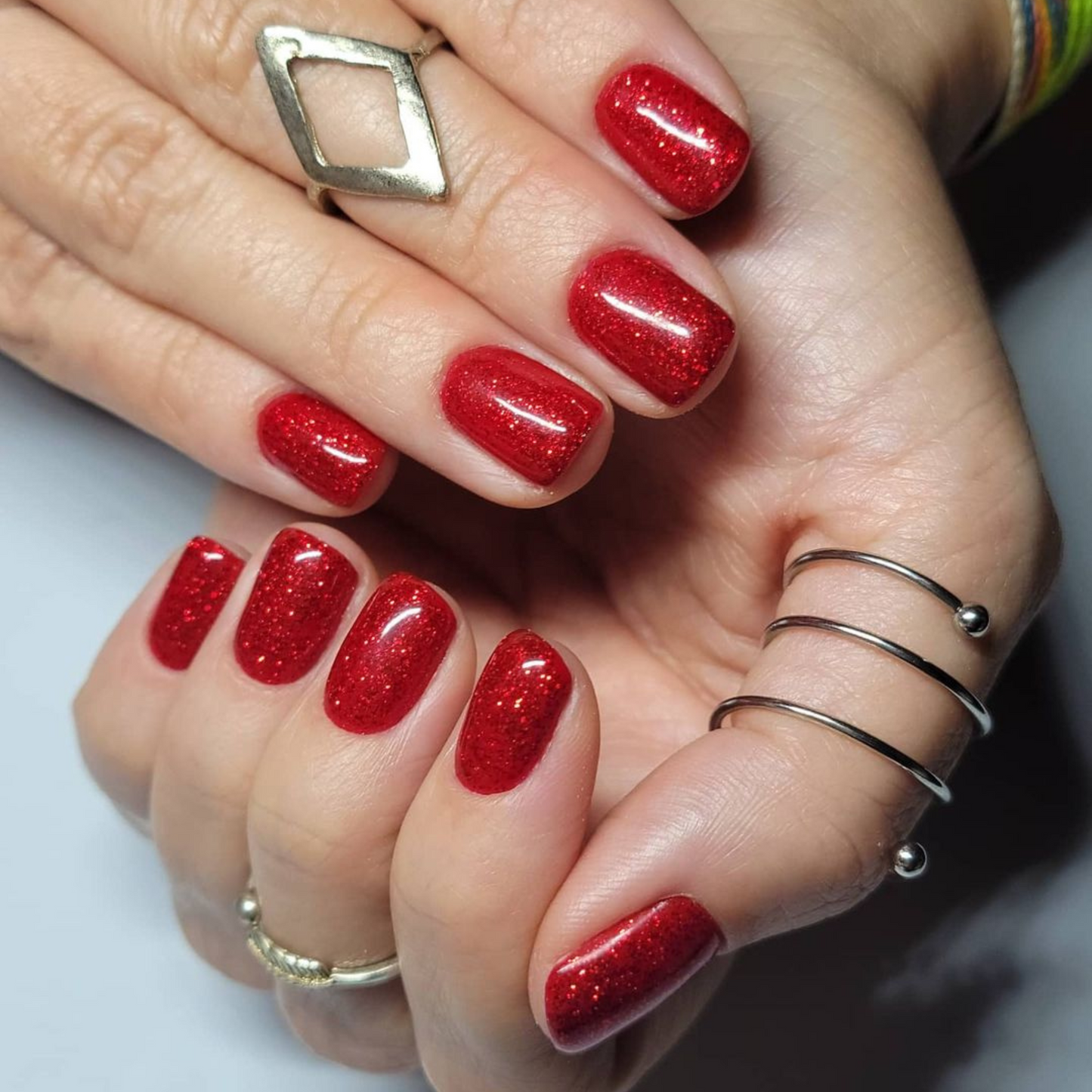 Hand with short square nails wearing Firework Star red glitter nail polish