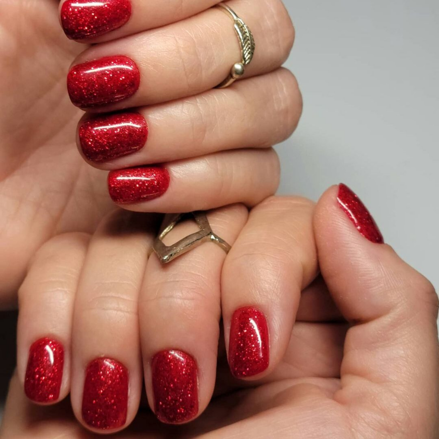 Hand with short square nails wearing Firework Star red glitter nail polish