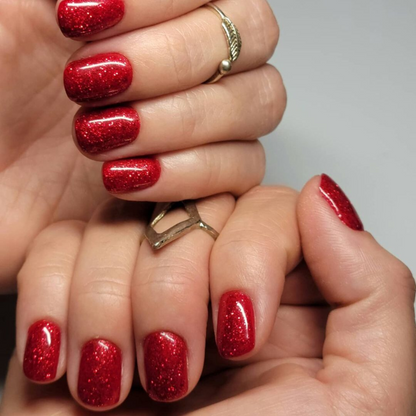 Hand with short square nails wearing Firework Star red glitter nail polish
