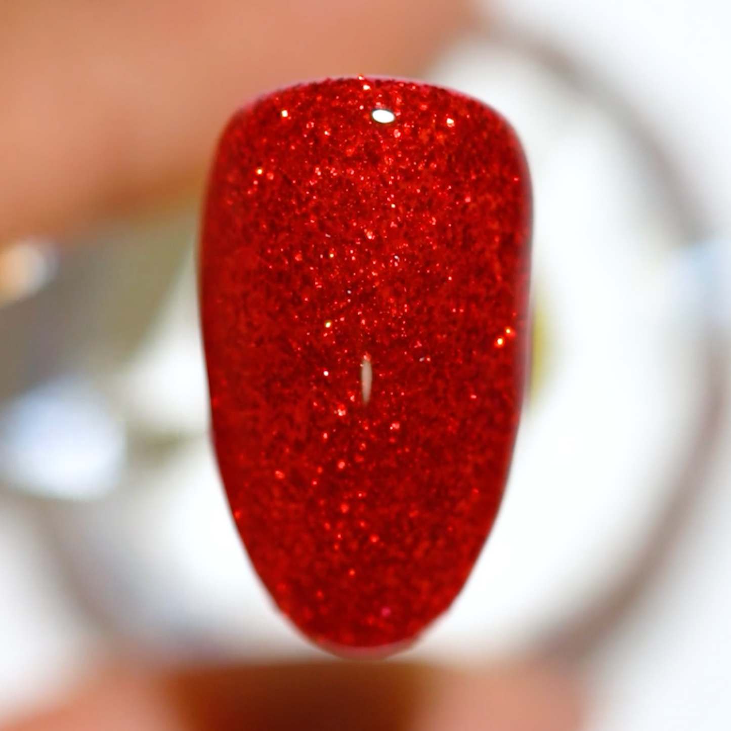 Color swatch on short almond nail tip wearing Firework Star red glitter nail polish