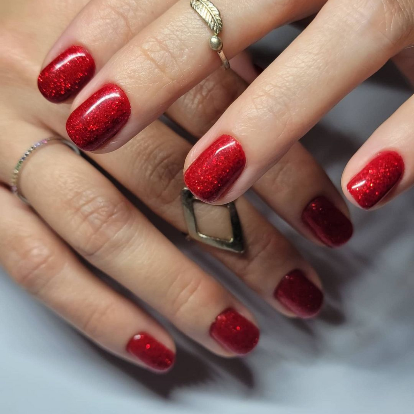 Hand with short square nails wearing Firework Star red glitter nail polish