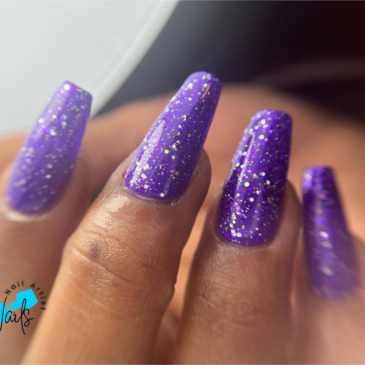 Hand with long coffin nails wearing Lush Lilac Star purple glitter nail polish with silver flecks