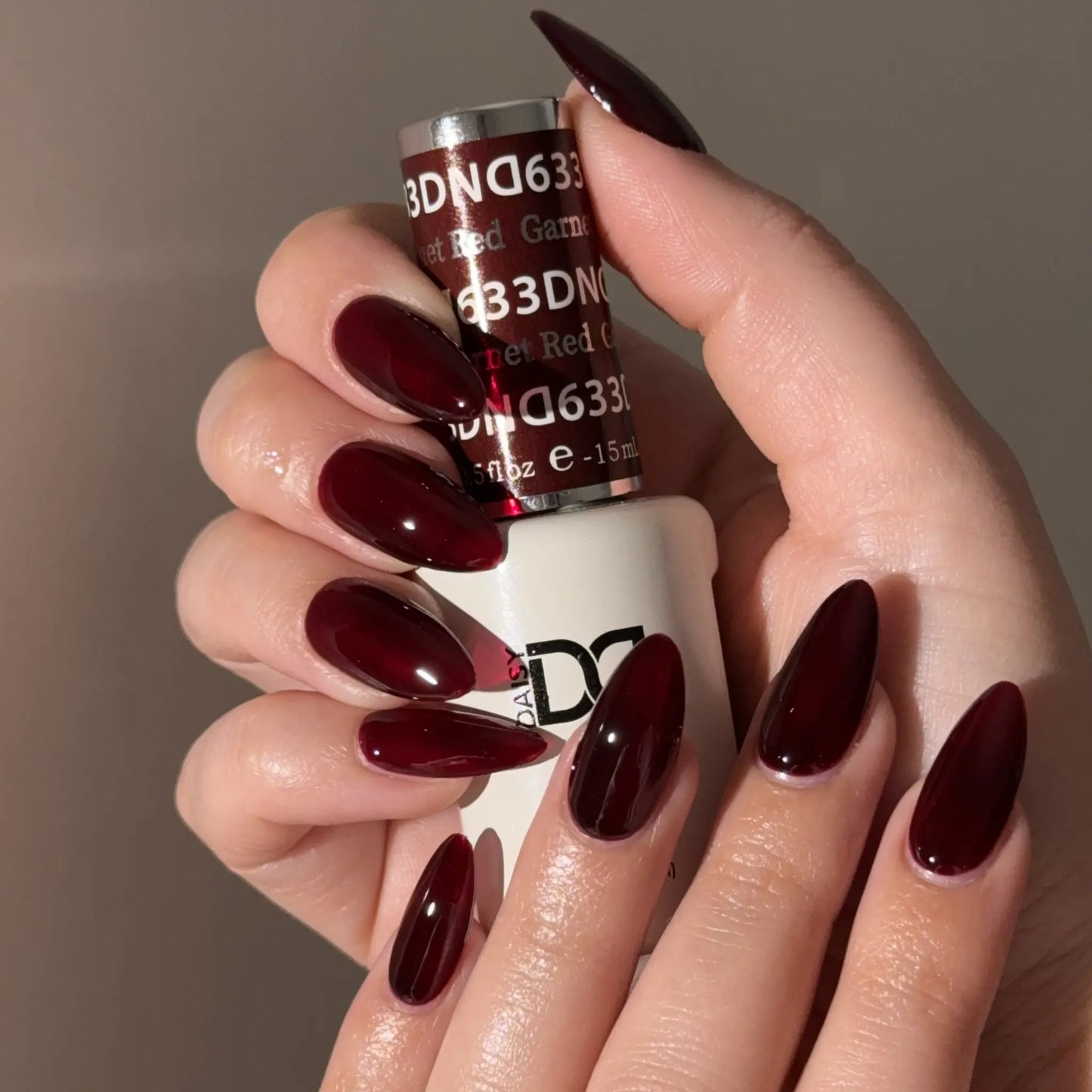 Hand with dark red nail polish holding a bottle of DND nail polish.