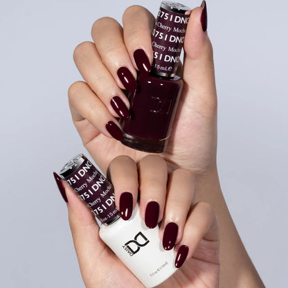 Hand with popular Cherry Mocha dark red brown nail polish holding DND nail polish bottles against a light gray background