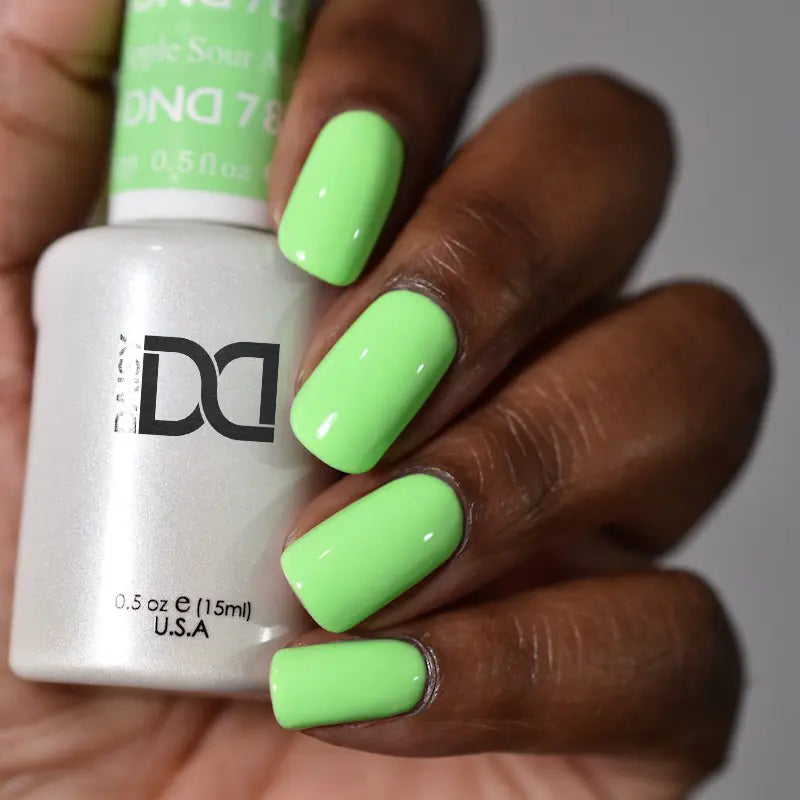 Hand with medium square/oval nails wearing sour apple neon pastel green nail polish, holding a bottle of DND nail polish