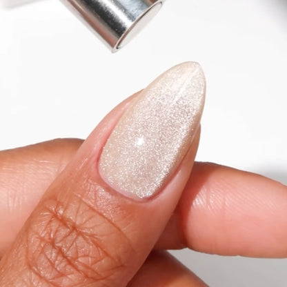 Finger with medium almond nails wearing toe beans light champagne cat eye nail polish