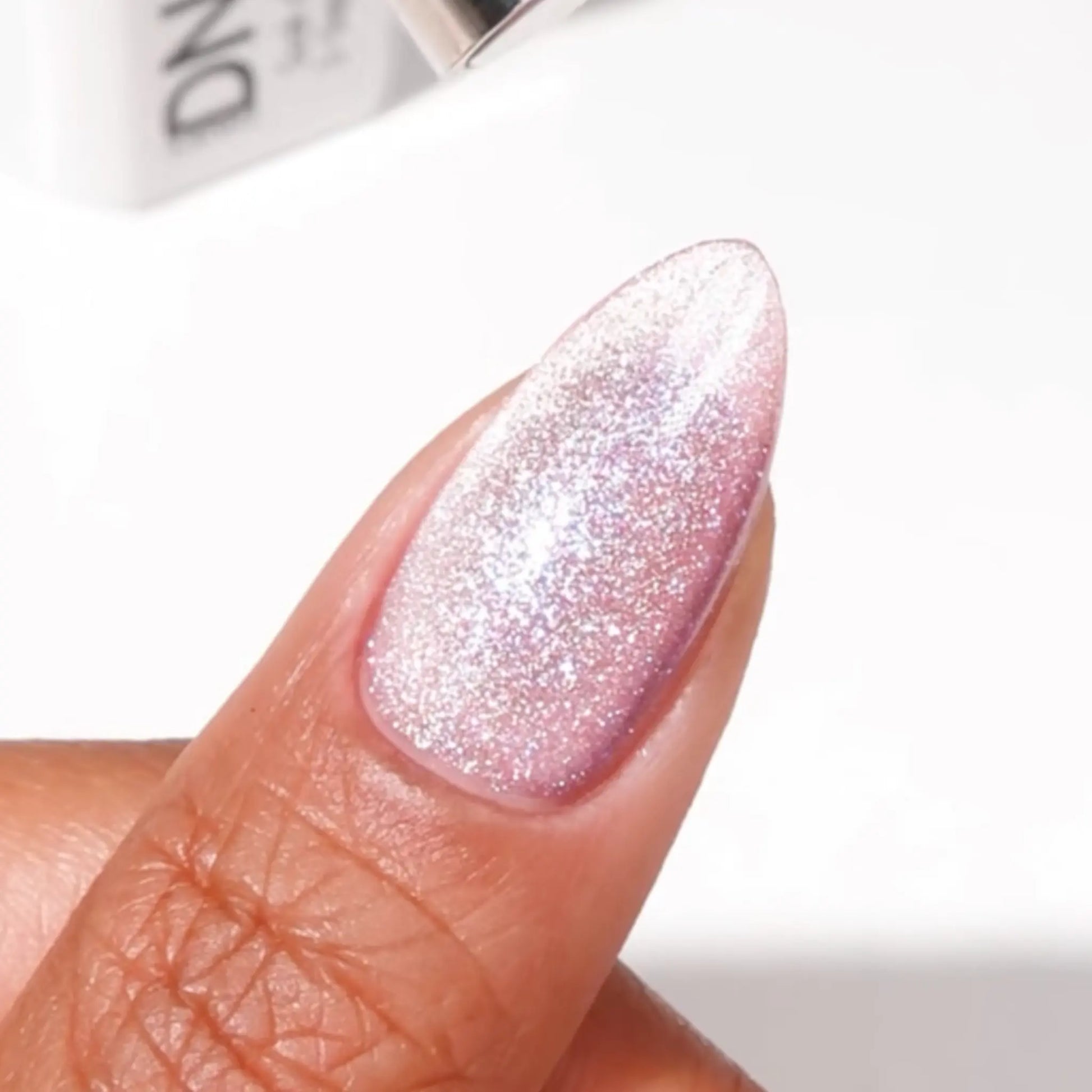 Finger with medium almond nails wearing karma is a cat mauve purple pink cat eye nail polish and iridescent glitter