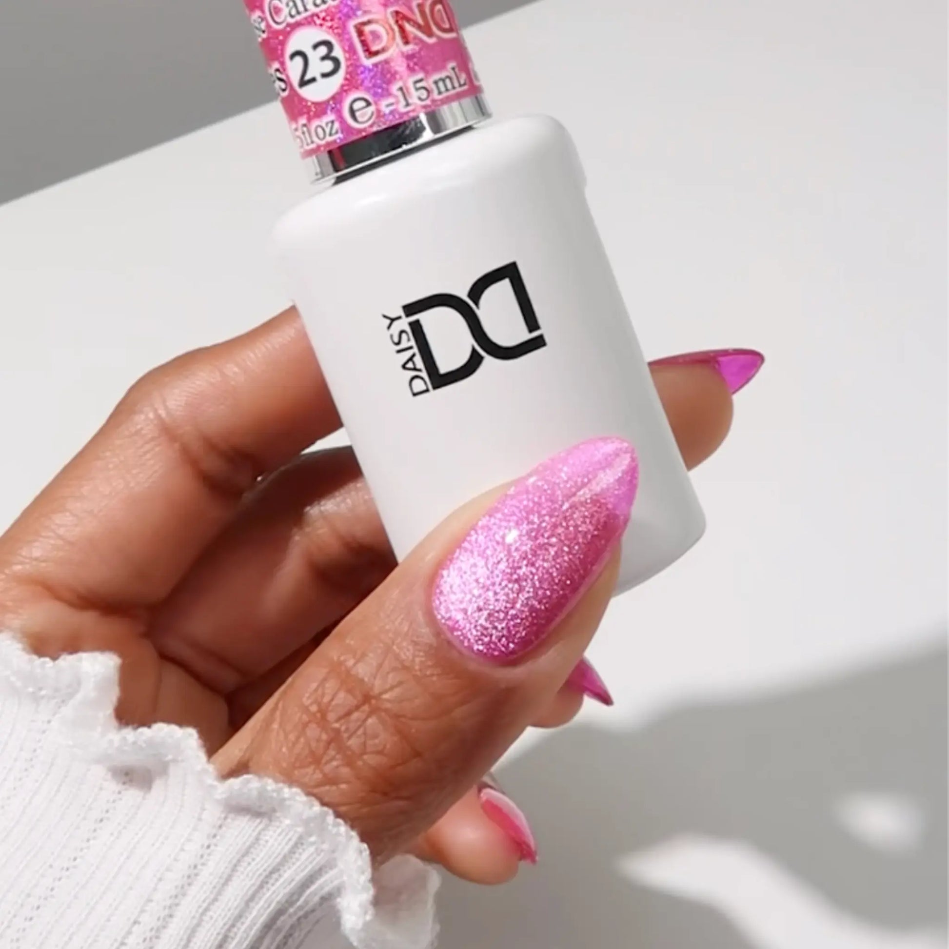 Hand with medium almond nails wearing rose carat glittery bright pink cat eye nail polish, holding a bottle of DND nail polish