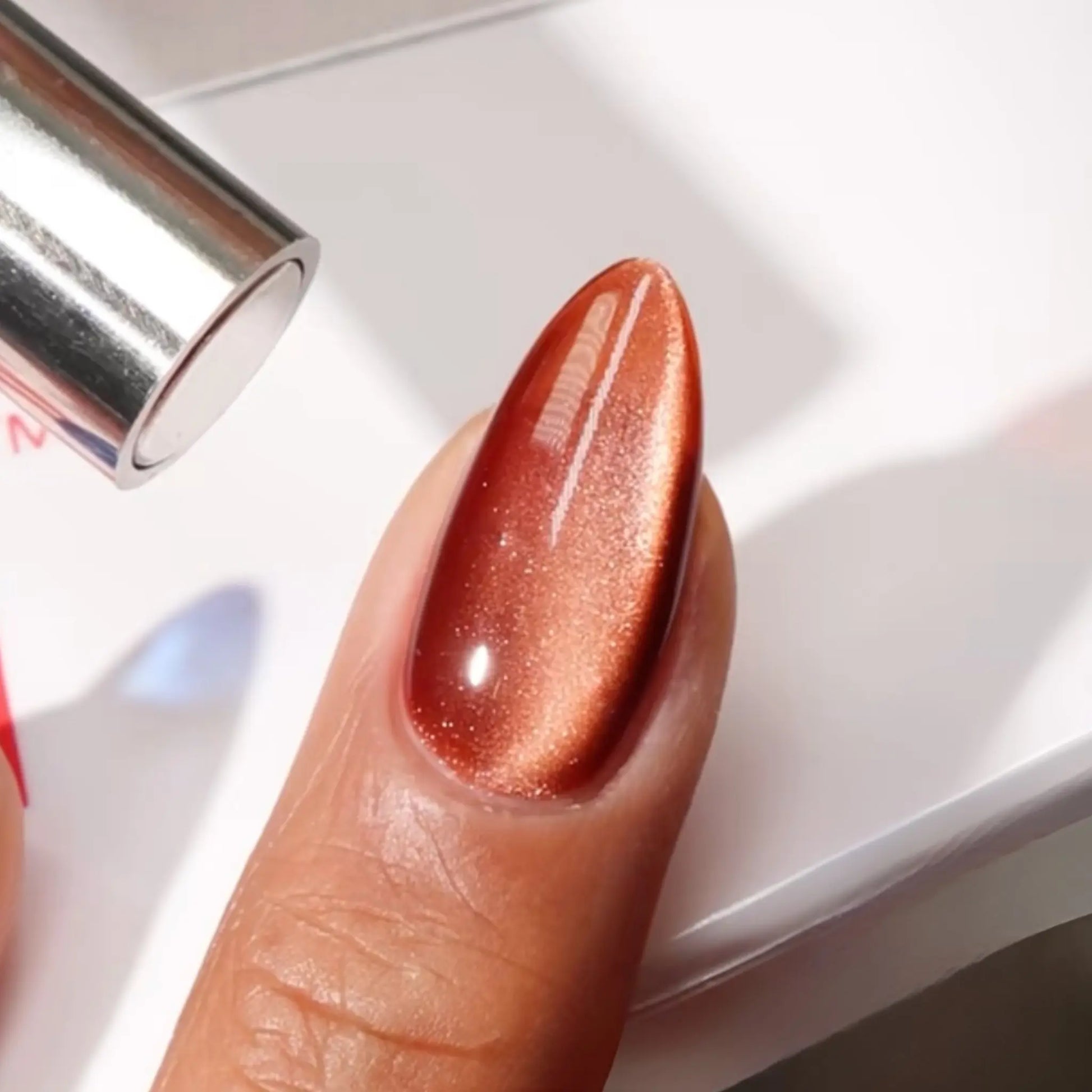 Finger with medium almond nails wearing Affogato brown caramel cat eye nail polish with magnetic effects