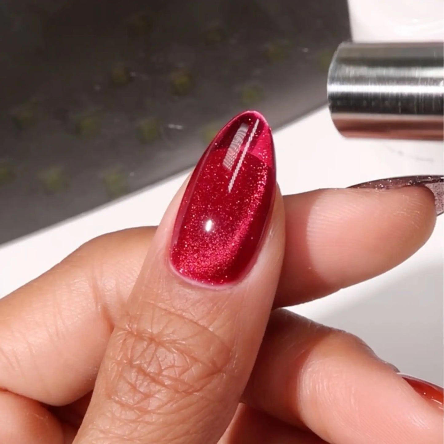 Finger with medium almond nails wearing lucky cat red berry cat eye nail polish with magnetic effects