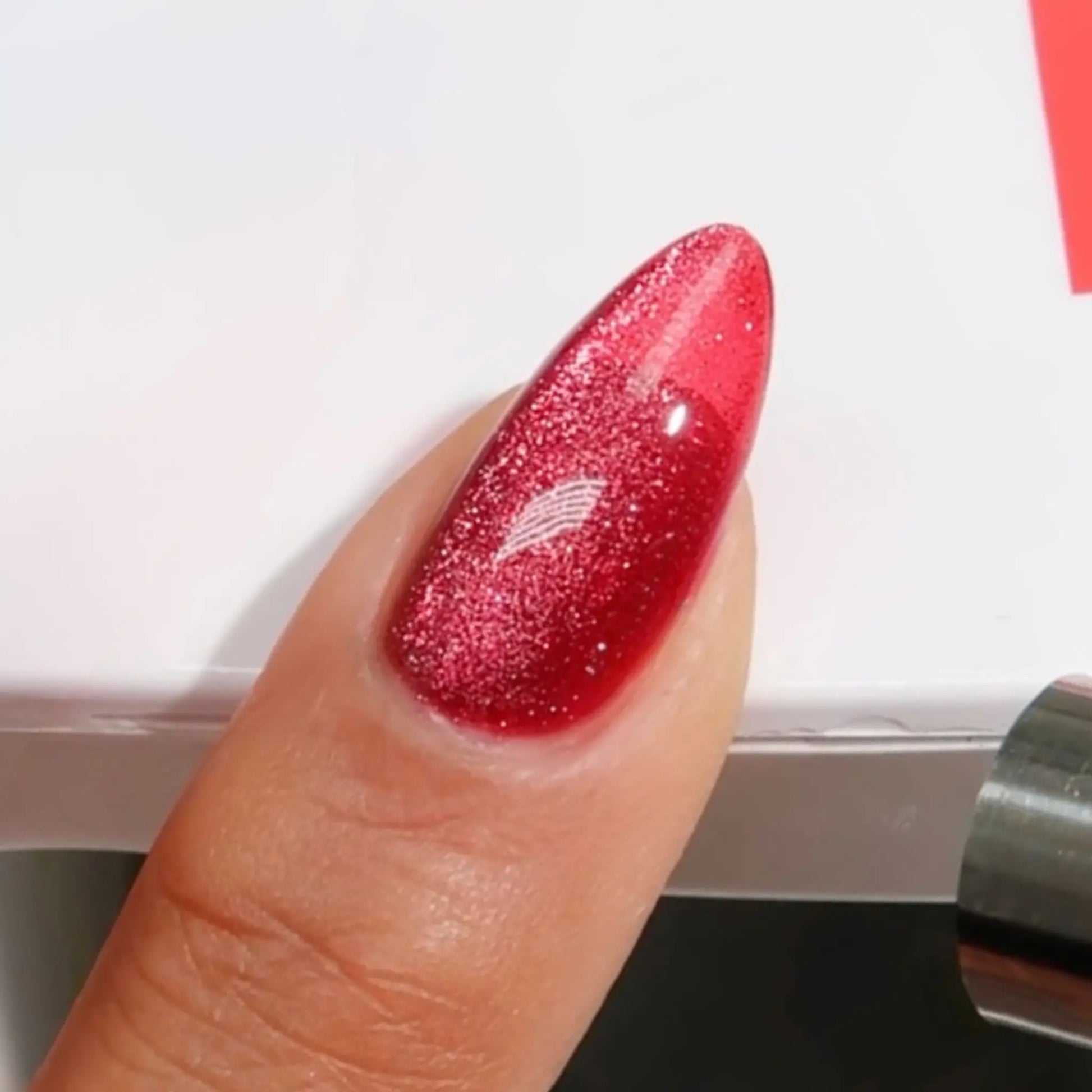 Finger with medium almond nails wearing meowroon pinkish red cat eye nail polish with magnetic effects