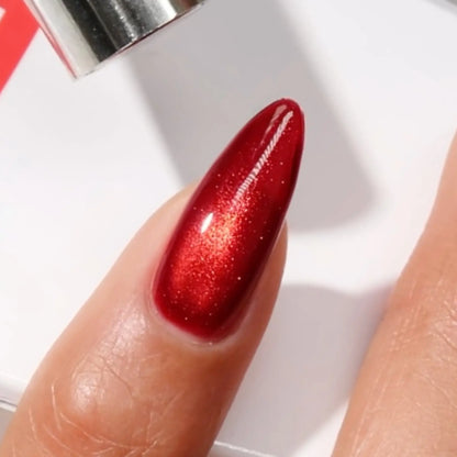 Finger with medium almond nails wearing wild cat red a warm crimson cat eye nail polish with magnetic effects