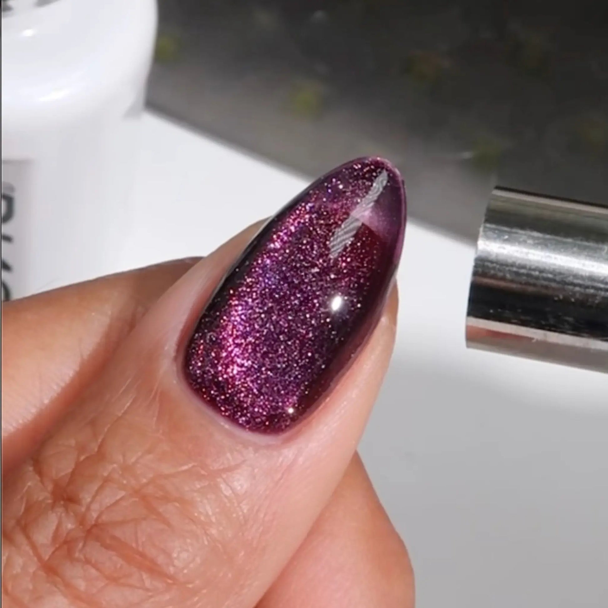 Finger with medium almond nails wearing cheshire cat smile purple cat eye nail polish with magnetic effect