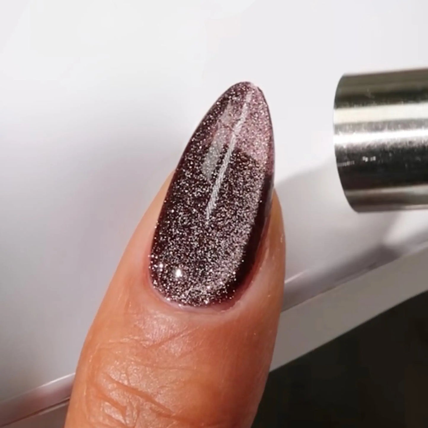 Finger with medium almond nails wearing the black cat black cat eye nail polish with grey magnetic effect