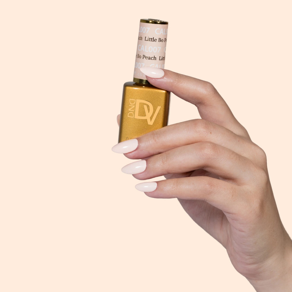 Hand holding gold-capped bottle labeled Little Bo Peach, peach background