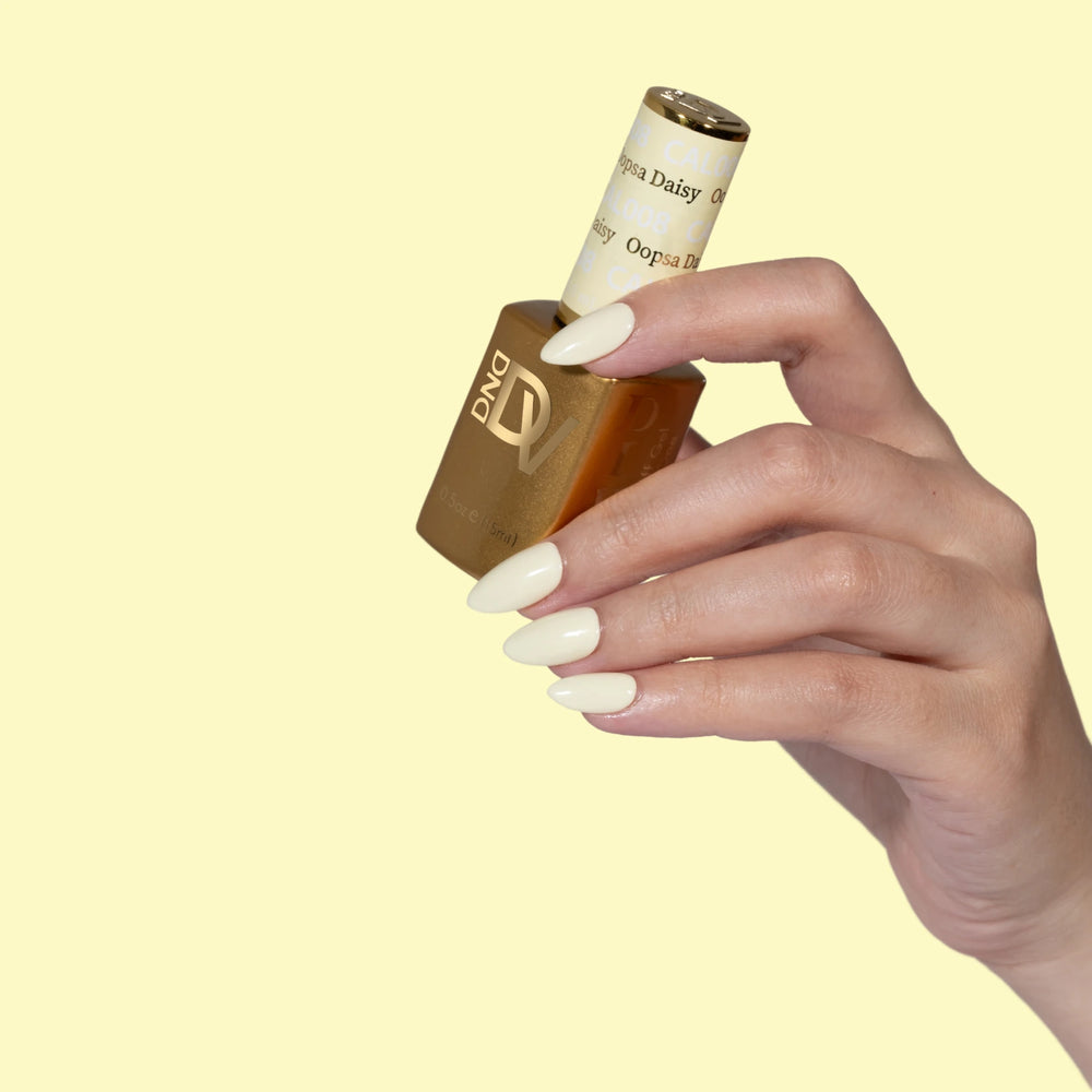Hand holding gold-capped bottle labeled Oopsa Daisy, pale yellow background