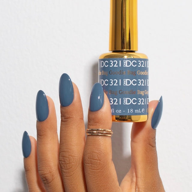 Hand with dusty blue-gray nails holding DND DC #321 gel bottle