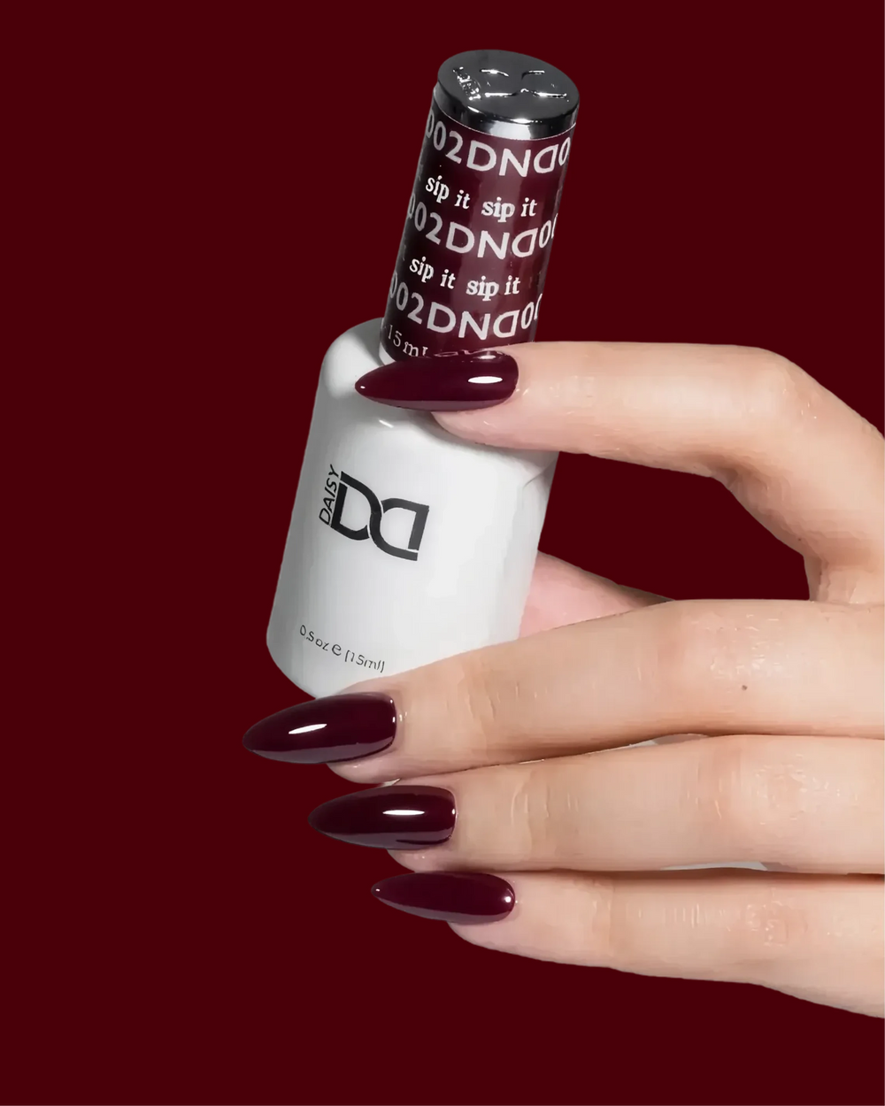 Hand with dark burgundy nails holding a DND gel polish bottle labeled "Sip It"