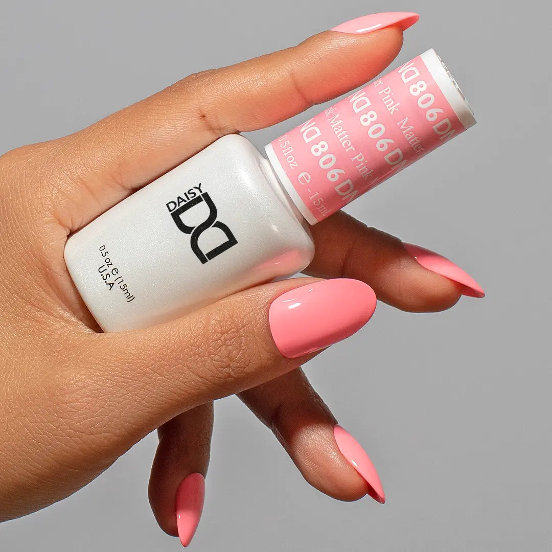 Hand with short medium round almond nails in a light coral pink color, holding a DND nail polish bottle