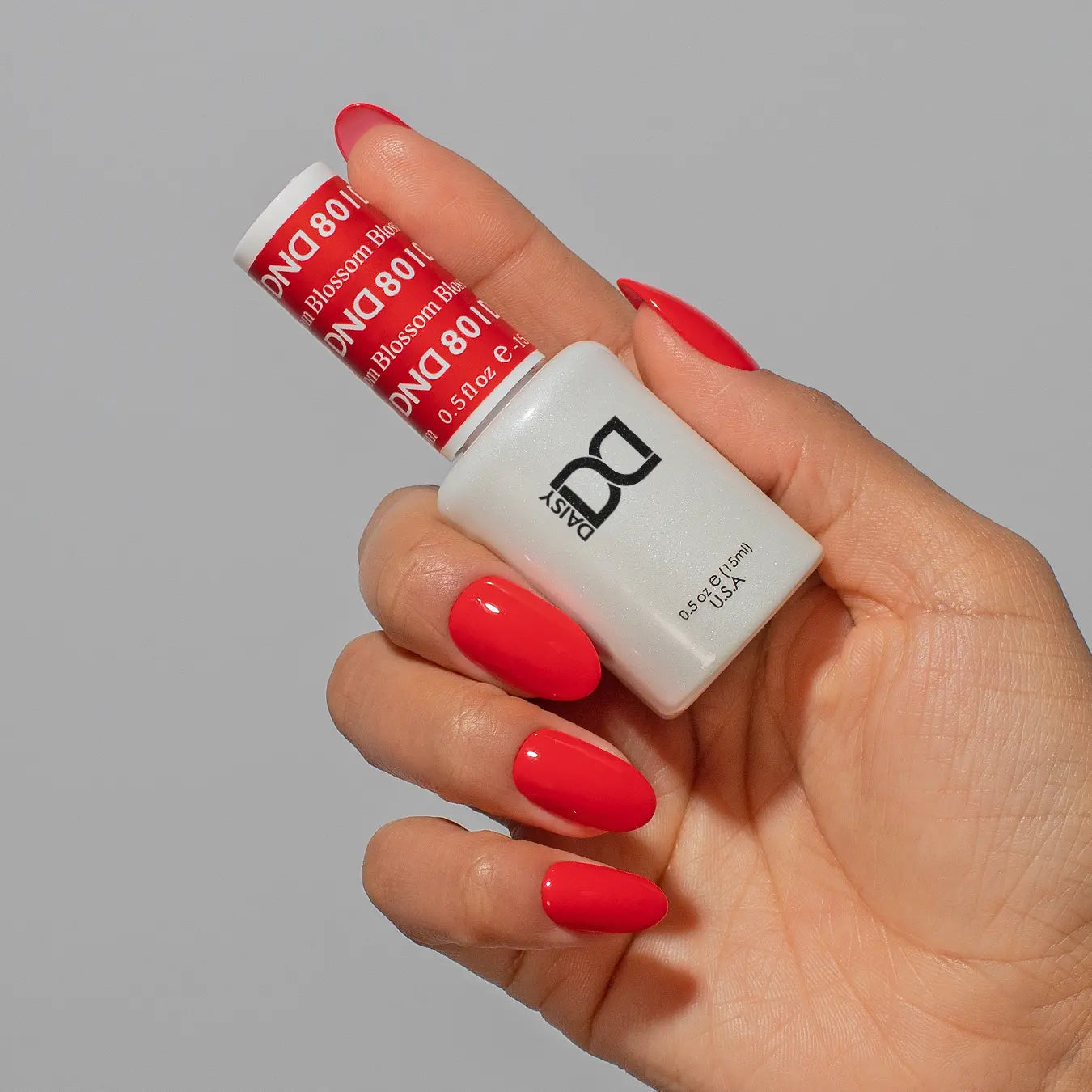 Hand holding a bottle of DND red nail polish on medium round nails