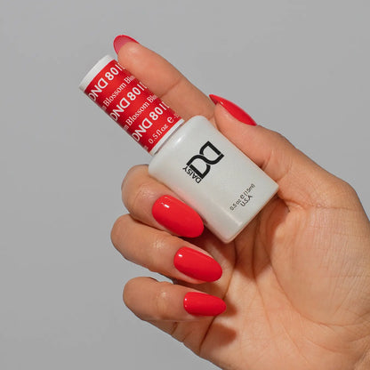 Hand holding a bottle of DND red nail polish on medium round nails