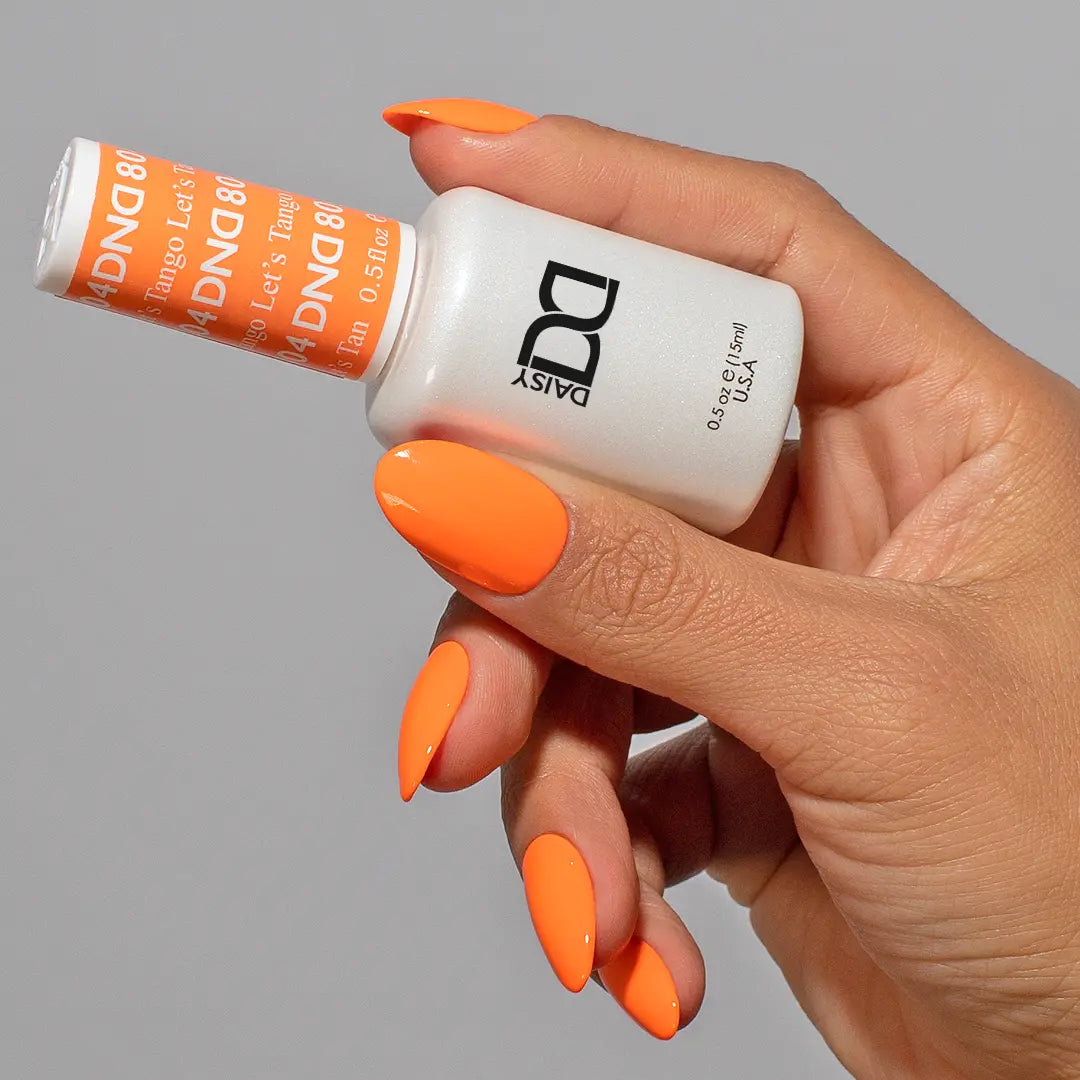 Hand holding a bottle of DND orange nail polish with medium round almond nails