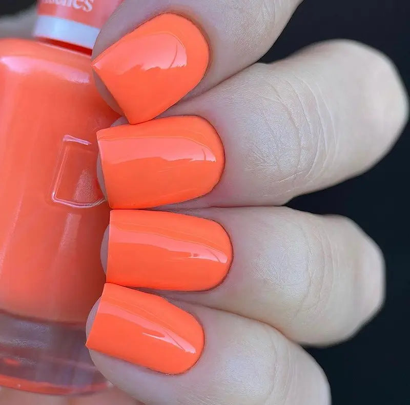 Hand with medium square nails wearing peaches n cream bright orange nail polish, holding a matching bottle of DND nail polish